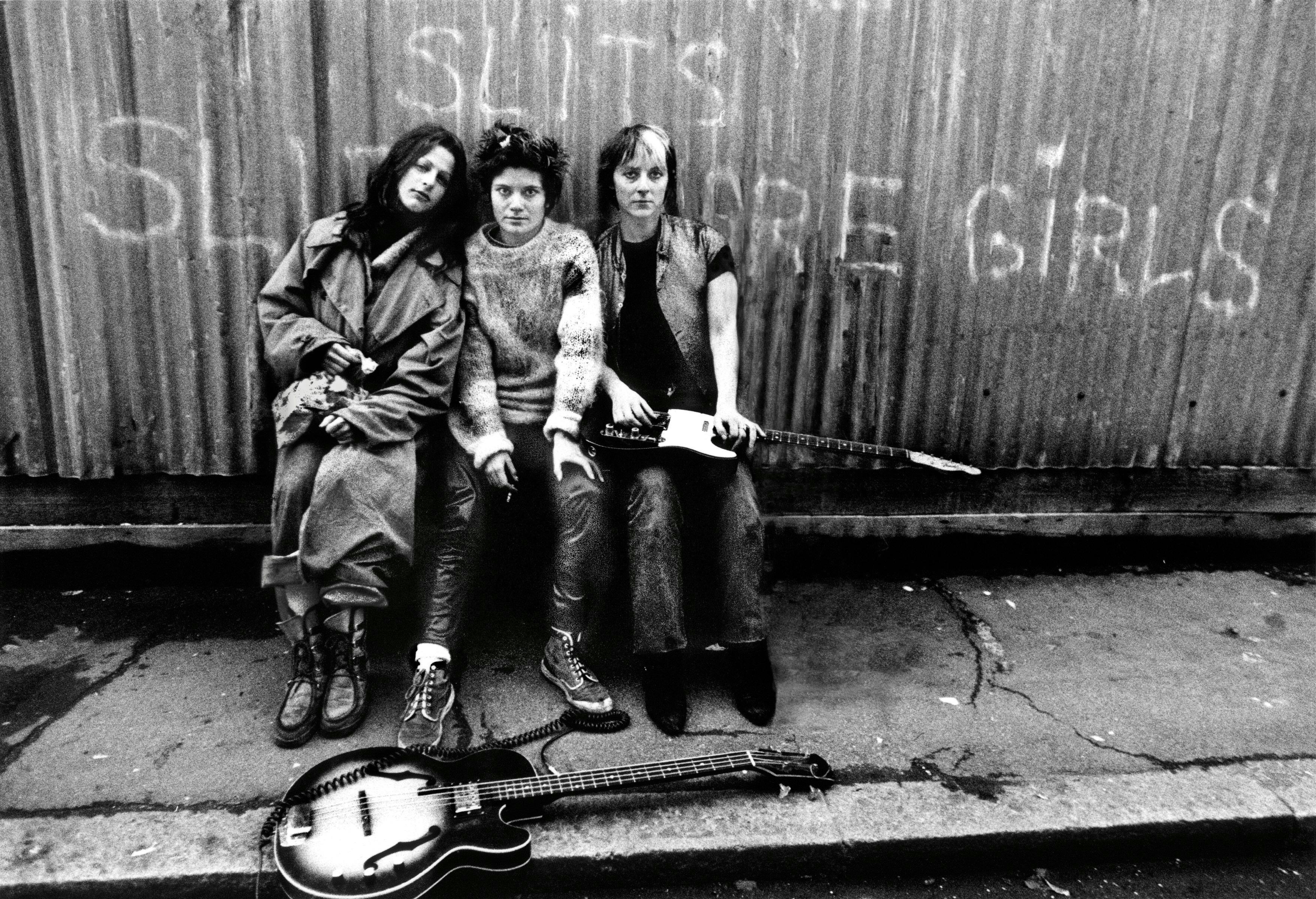 1977 huty 19484 huty19484 huty1948433 bass guitar black and white day drummer electric guitar fence full length grafitti guitarist looking at camera only women outdoors pop musician punk rock singer sitting street the slits three people western script person human guitar musical instrument leisure activities